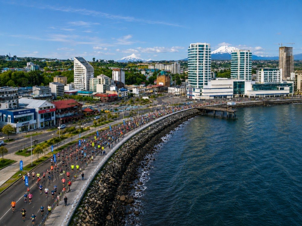 Corredores por la costanera de Puerto Montt al atardecer, con la ciudad y el volcán Osorno al fondo